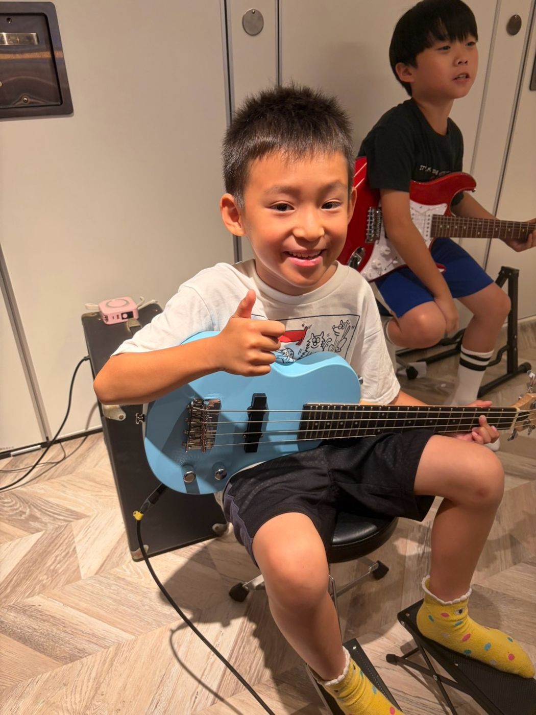 孩子抱著淺藍色 Bass，後面有人彈電吉他